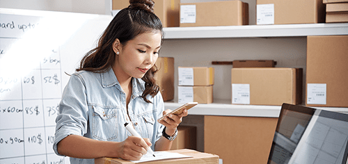 Young entrepreneur checking inventory on smartphone in a small business warehouse.