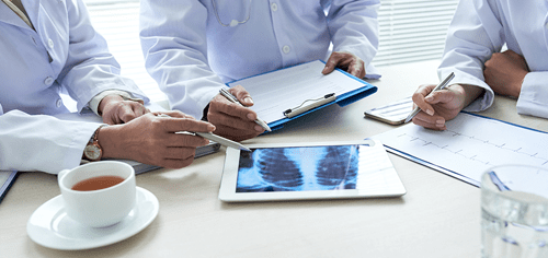 Medical professionals discussing patient information with digital tablet and x-rays on the table.